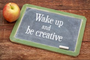 Wake up and be creative  - inspirational positive words on a slate blackboard against red barn wood